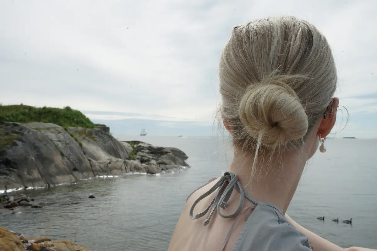 Low twist-and-wrap bun hairstyle with coastal cliffside and sea in the background