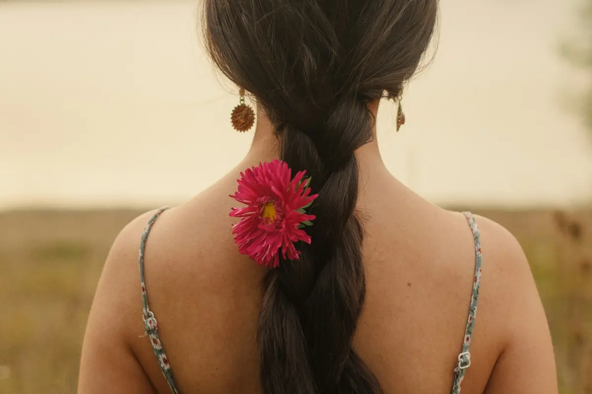 Loose fishtail braid with floral hair accent, outdoor natural light