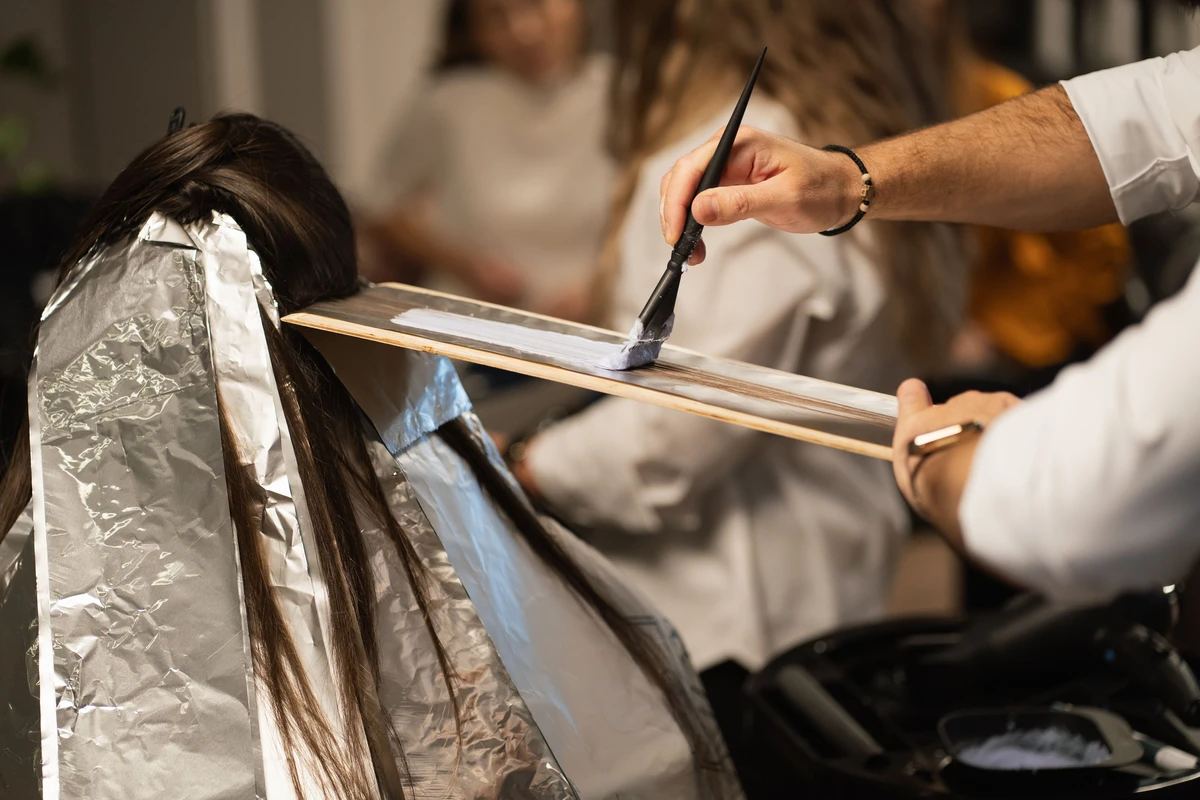 Hair colorist painting balayage color onto a client's hair, close-up on hands
