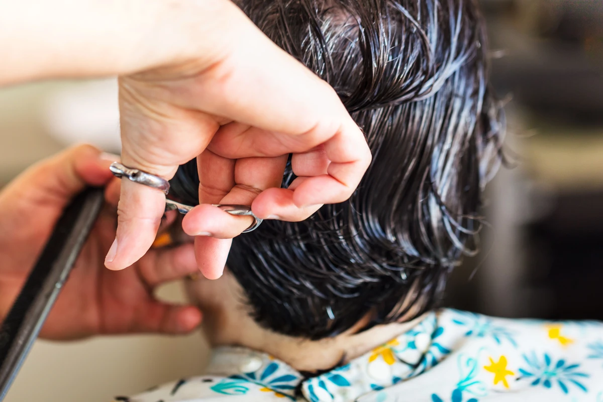 Hairstylist cutting a client's short pixie haircut in a salon, close-up on hands