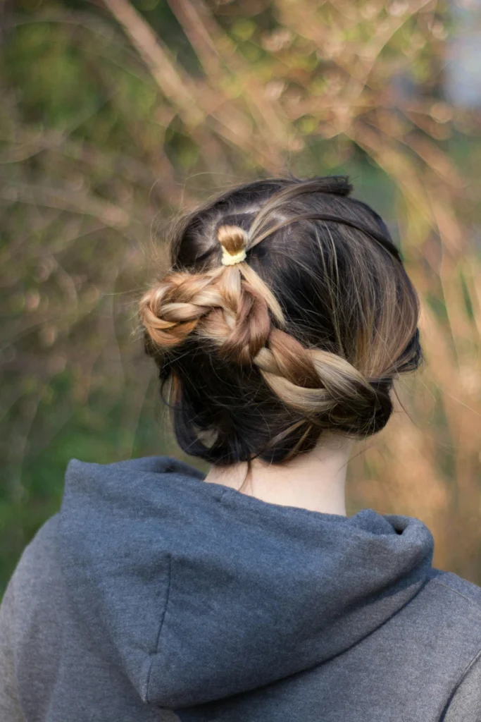 Braided low bun at the nape on lob-length hair, outdoor back view