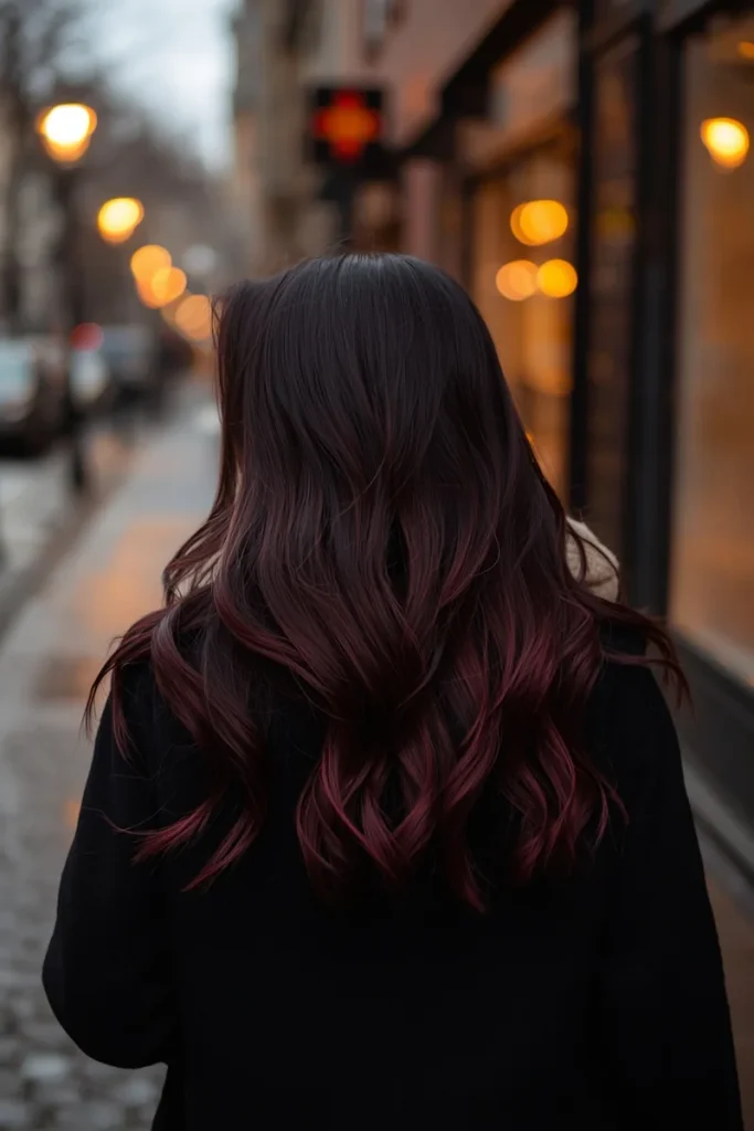 Long black cherry waves with a deep red-violet shimmer on a woman walking down a city street on a winter evening