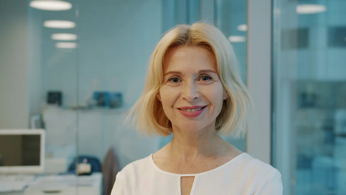 Smiling woman over 50 with a jaw-length blonde bob with soft flipped ends in a bright office