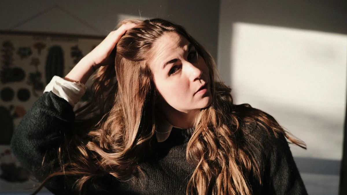 Woman running her hand through long wavy hair as it grows out past a bob