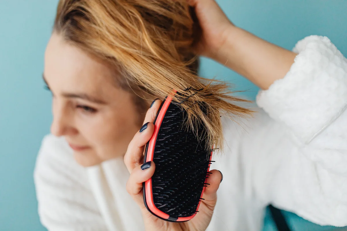 Close-up of a woman brushing damaged hair with visible split ends caught in the brush bristles