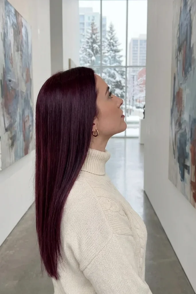 Long sleek merlot wine red hair on a woman in a cream turtleneck admiring abstract art in a bright gallery with snow outside
