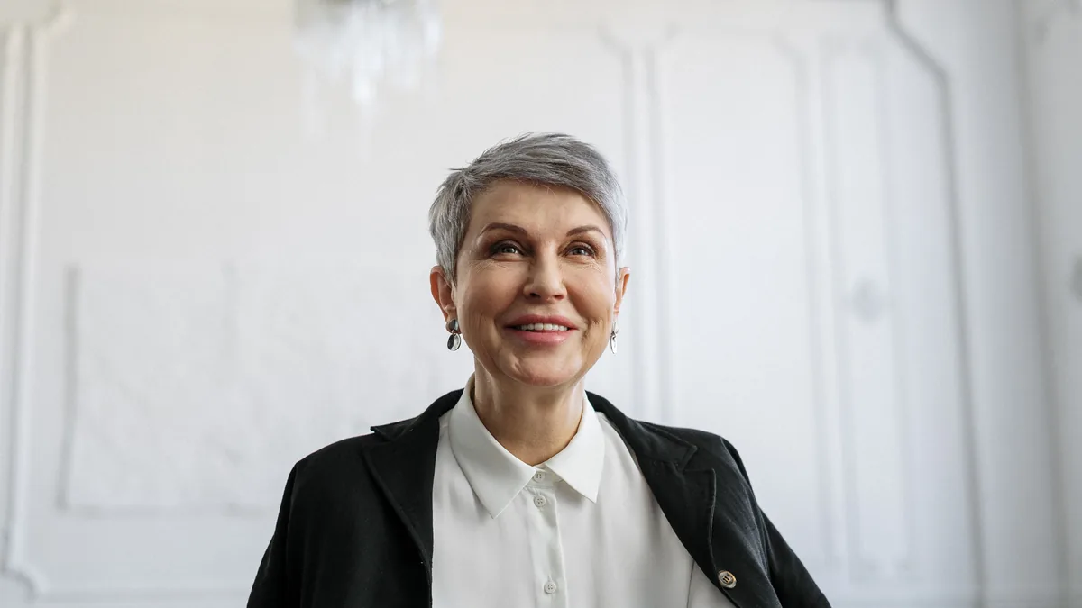 Smiling woman over 50 with a short tapered silver pixie cut in a black blazer and white shirt