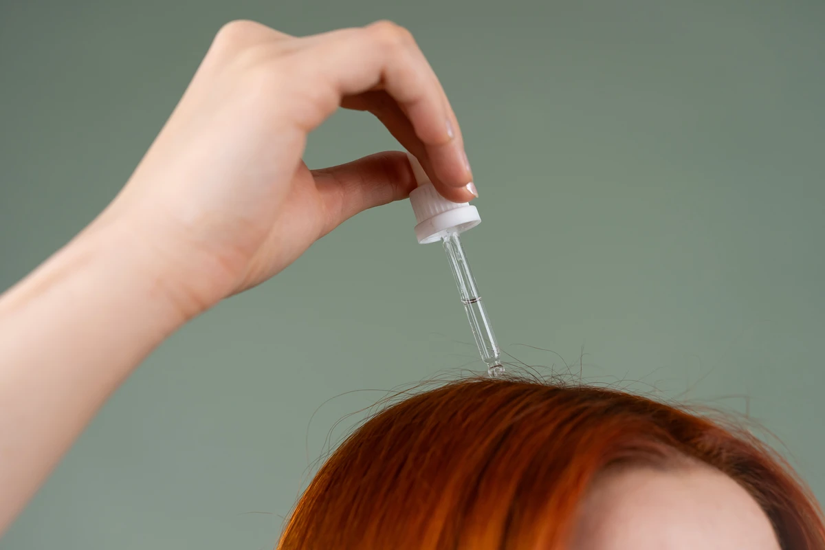 Close-up of a dropper applying scalp treatment serum directly to the roots at the hairline