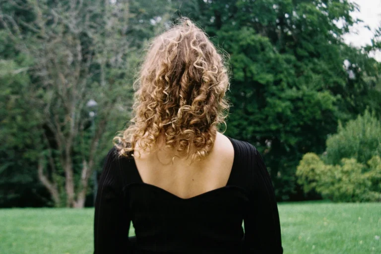 Woman with layered wavy shag haircut, back view, textured hair against green outdoor background