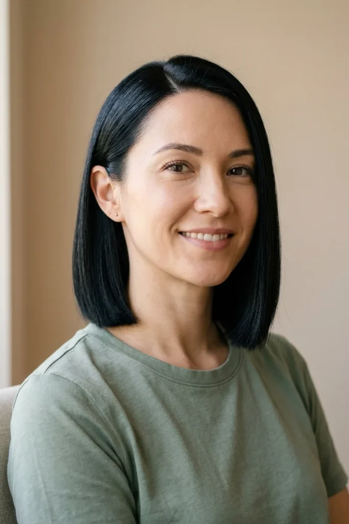 Woman with fine, straight black hair in a one-length blunt bob just below the chin, one side tucked behind her ear