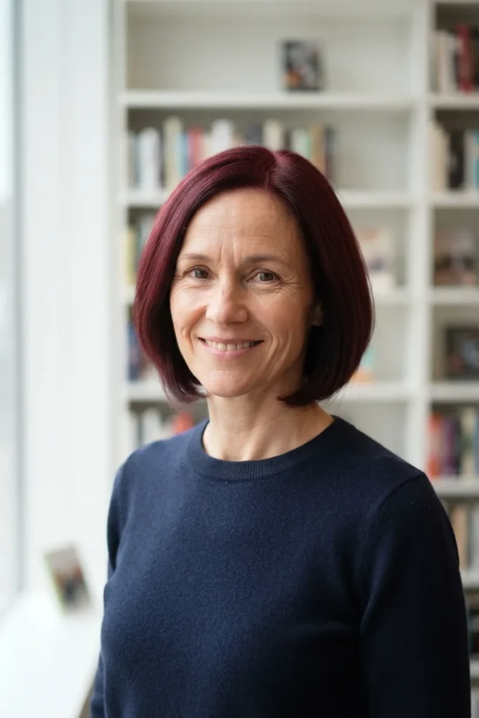 Woman in her 40s with a classic burgundy chin-length bob, smiling in a bright library
