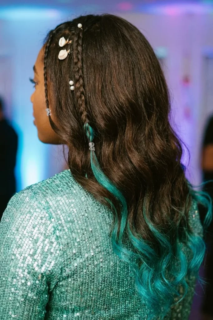 Woman with long brown waves, thin braids, shell and pearl clips and teal temporary color on the ends, back three-quarter view at a party