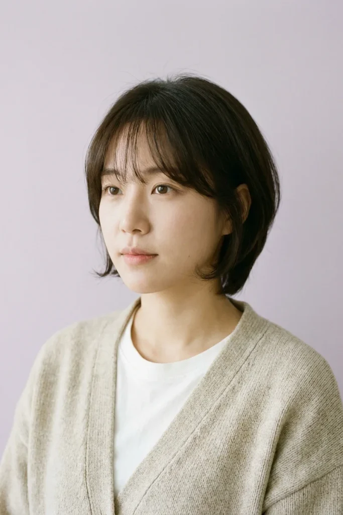 Woman with dark brown hair in a Korean-style short wolf cut with sheer see-through bangs, a rounded crown and ends curling inward at the jaw