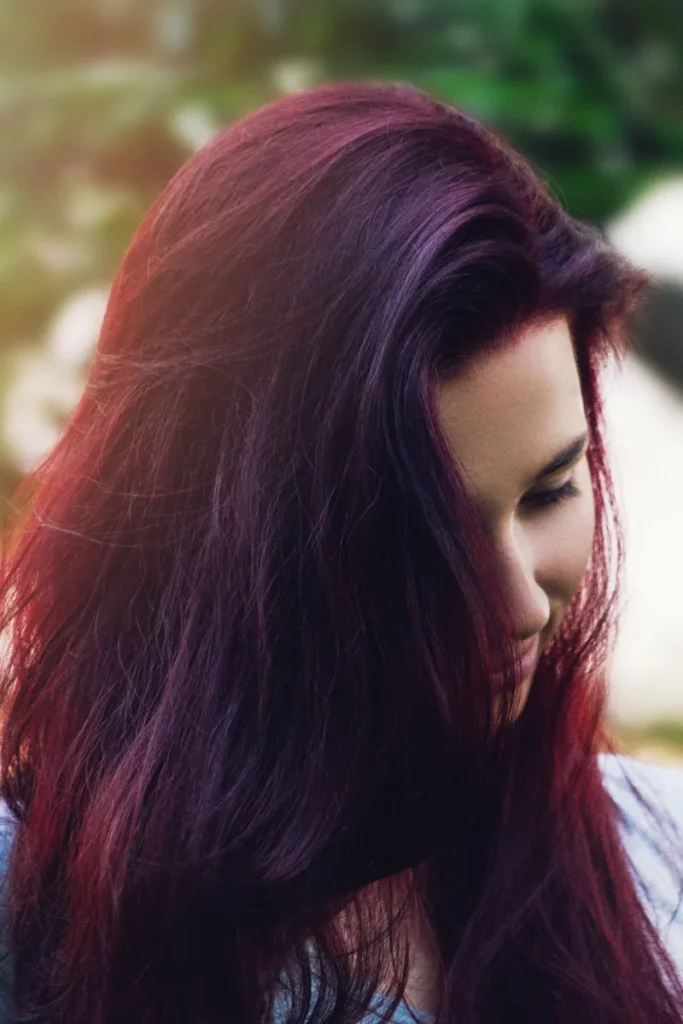 Woman with long plum burgundy hair with violet tones, looking down in soft outdoor light