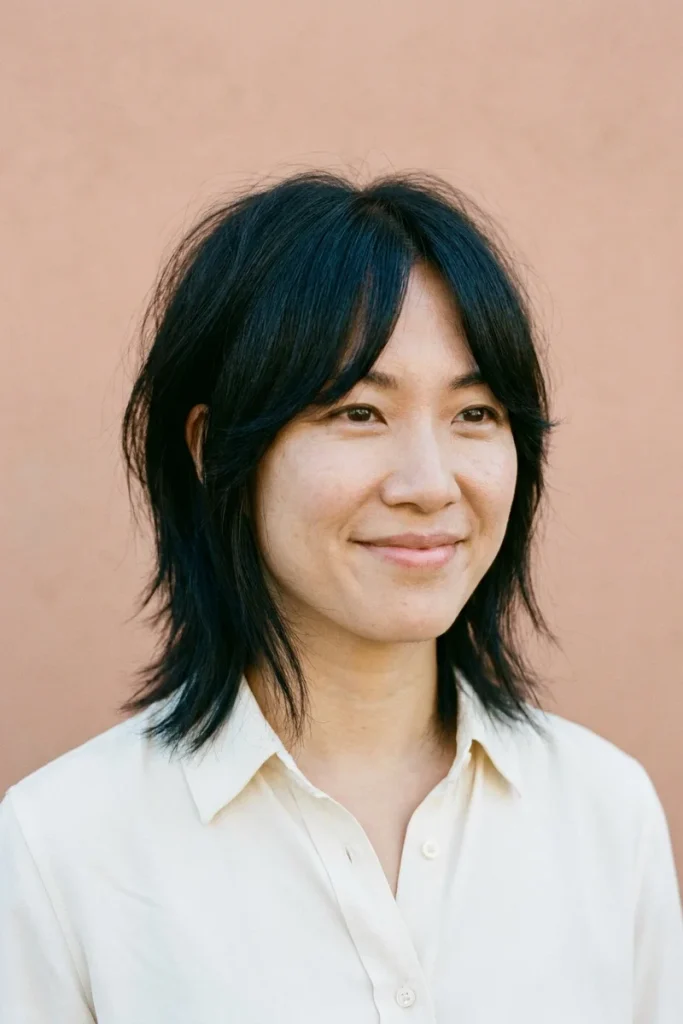 Woman with black hair in a short wolf cut with center-parted curtain bangs, choppy crown layers and piecey ends just below the jaw